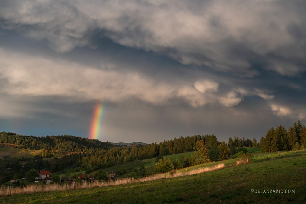 Rainbow over a forested landscape under storm clouds